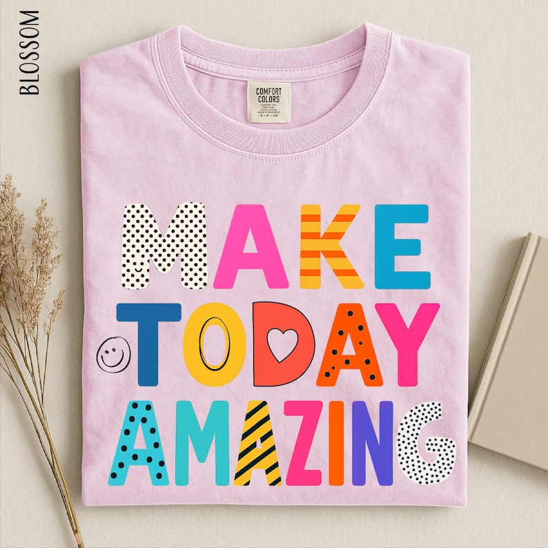 A pink t-shirt with the text "MAKE TODAY AMAZING" printed on it, along with various colorful and playful lettering designs.