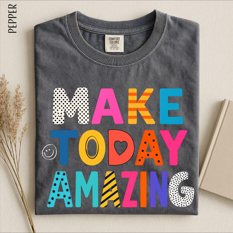A gray t-shirt with the text "MAKE TODAY AMAZING" printed on it in a colorful, playful font.