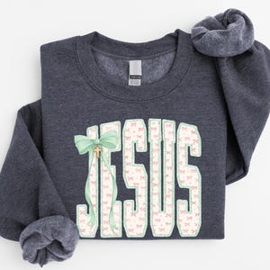A gray sweatshirt with the word "JESUS" printed in large letters, along with a bow and pink and white patterned fabric.