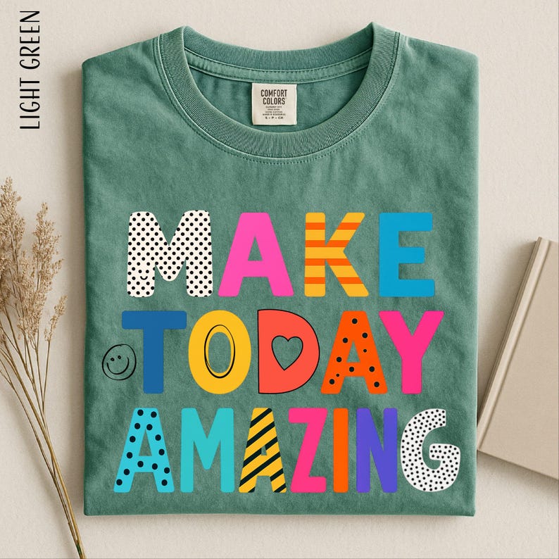 A green t-shirt with the text "MAKE TODAY AMAZING" printed on it, along with various colorful and playful lettering designs.