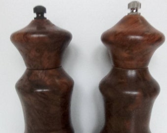 May include: A set of two wooden salt and pepper shakers with a dark brown wood grain finish. The shakers have a rounded top and a bulbous body.