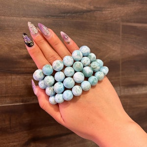 May include: A bracelet made of light blue and white gemstone beads. The beads are round and have a marbled appearance.
