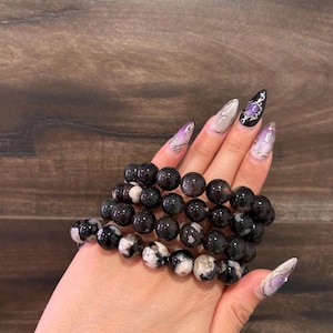 May include: A stack of four black and white agate beaded bracelets. The beads are round and have a natural, polished finish.