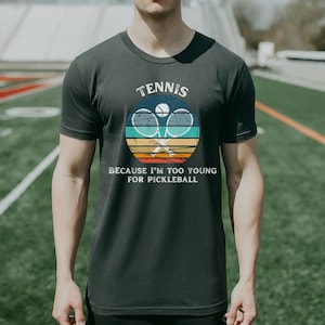 a man standing on a field wearing a tennis racket t - shirt