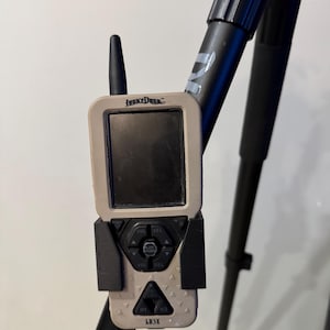 May include: A tan and black Lucky Duck LD3X electronic game caller is mounted on a black tripod. The caller has a screen, buttons, and an antenna. The tripod legs are black.