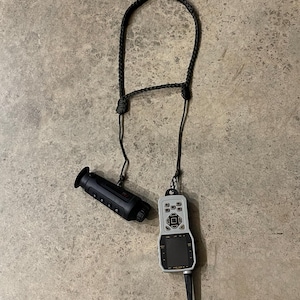 Könnte beinhalten: Ein schwarzer und grauer Entfernungsmesser mit einem schwarzen Band und einer Fernbedienung mit einem Bildschirm und Knöpfen.