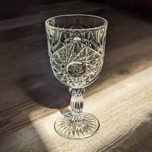 May include: A clear glass goblet with a cut glass design. The goblet has a round bowl and a tall stem with a wide base.