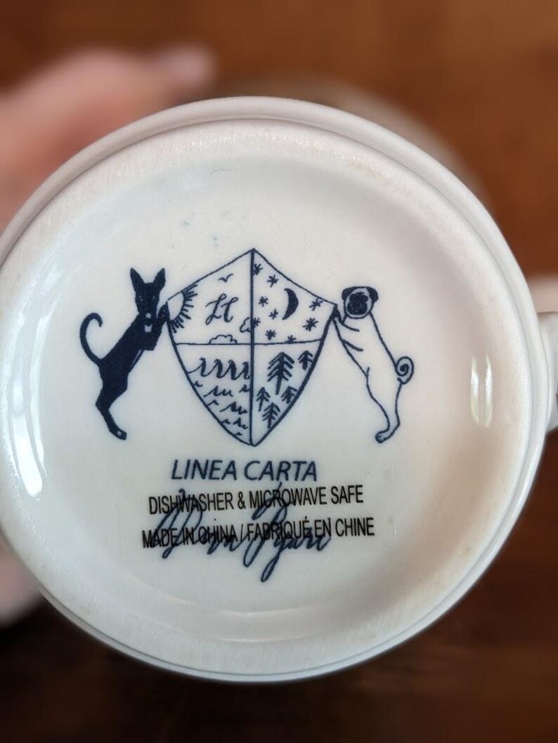 May include: White ceramic mug base with a navy blue illustration. A shield design is flanked by a black dog and a pug. The text "LINEA CARTA" and "DISHWASHER & MICROWAVE SAFE" are printed below the illustration.