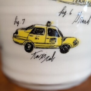 May include: White ceramic mug with a yellow taxi cab illustration. The taxi has black wheels and windows, with the word "taxicab" written below. The mug also has handwritten text, including "fig. 6" and "fig. 7".