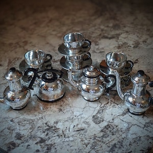 May include: A silver tea set with black handles. The set includes a teapot, creamer, sugar bowl, and three cups and saucers.