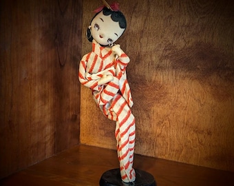 Muñeca geisha japonesa vintage con ojos grandes, pendientes dorados, kimono de rayas rojas, faja dorada y abanico de bambú en el pelo.