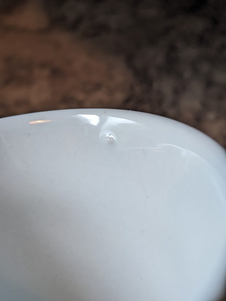 May include: A white ceramic mug with a small chip on the inside rim.