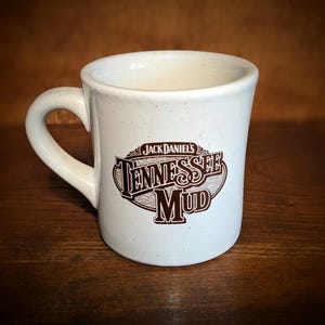 May include: White ceramic mug with a brown logo that says "Jack Daniel's Tennessee Mud".