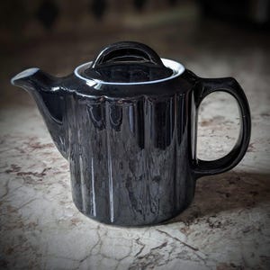 May include: A black ceramic teapot with a white rim and a fluted design. The teapot has a handle and a lid.