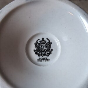 May include: White ceramic mug with a black and white crest featuring a crown and the letters "NH" with the text "Exclusive" underneath. The bottom of the mug reads "Dishwasher, microwave safe MADE IN CHINA."