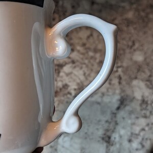 May include: White ceramic mug with a black stripe around the top and a white handle with a unique shape.