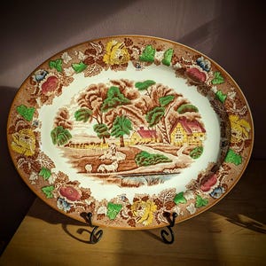 May include: A white ceramic mug with a black handle and the text "But First, Coffee" in a bold, black font. The mug is set against a blurred background, suggesting a cozy setting.