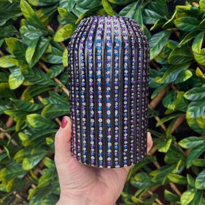 May include: A black vase with a textured surface, decorated with rows of iridescent rhinestones in shades of purple, blue, and silver.