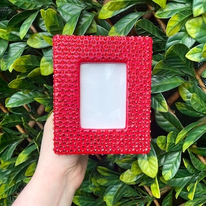 May include: A red picture frame covered in small red rhinestones. The frame is empty and ready for a photo.
