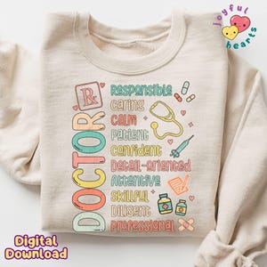 May include: A beige sweatshirt featuring a graphic design that reads "DOCTOR" in colourful letters. The graphic also includes a stethoscope, a pill bottle, a bandage, and other medical symbols. The words "Responsible, Caring, Calm, Patient, Confident, Detail-oriented, Attentive, Skillful, Diligent, Professional" are also included in the graphic.