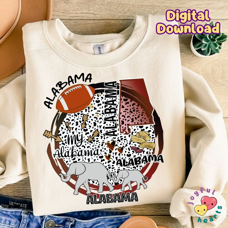 K&ouml;nnte beinhalten: Ein cremefarbener Pullover mit einem Grafikdesign, das den Bundesstaat Alabama, einen Elefanten, einen Football, Erdn&uuml;sse und die Worte "My Alabama" zeigt.