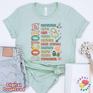 May include: A light green t-shirt with the word "DOCTOR" spelled vertically in colourful letters. The word is surrounded by words describing the qualities of a doctor, such as "responsible", "caring", "calm", "patient", "confident", "detail-oriented", "attentive", "skillful", "diligent", and "professional".