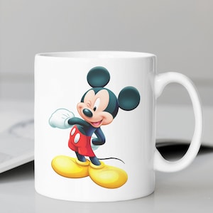May include: White ceramic mug featuring a cartoon image of Mickey Mouse wearing red shorts and yellow shoes. Mickey Mouse is winking and has a big smile.