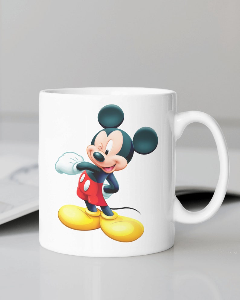 May include: White ceramic mug featuring a cartoon image of Mickey Mouse wearing red shorts and yellow shoes. Mickey Mouse is winking and has a big smile.