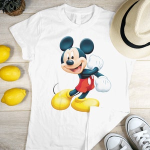 May include: White t-shirt featuring a cartoon image of Mickey Mouse in a red and yellow outfit. Mickey Mouse is smiling and waving.