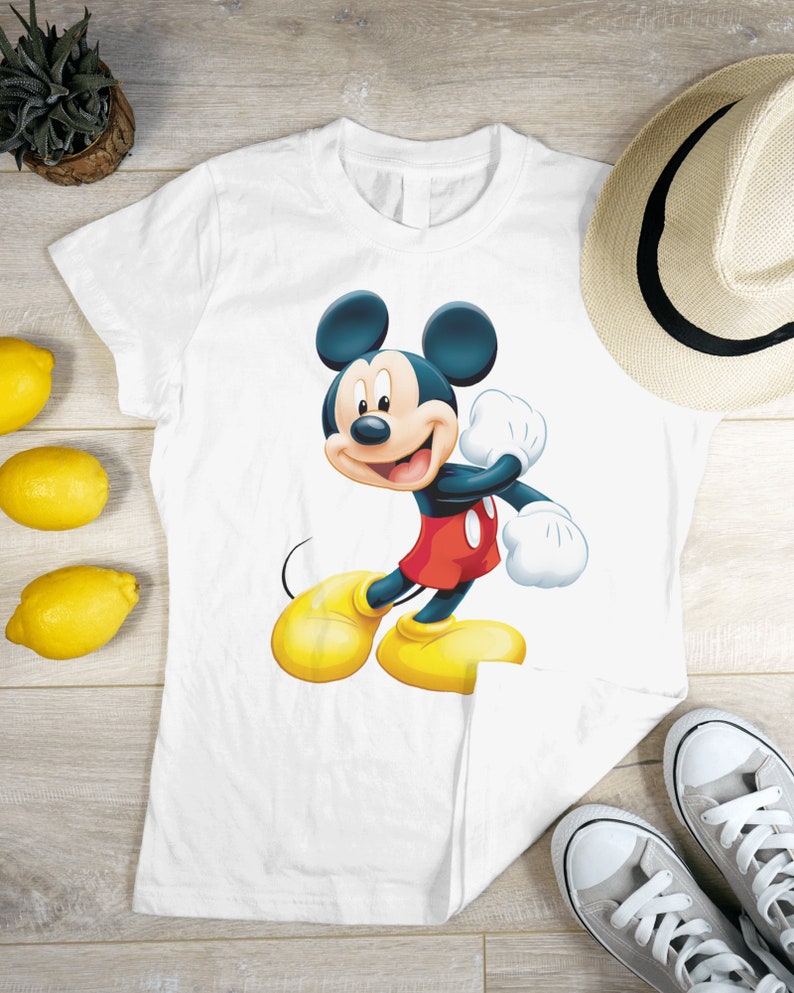 May include: White t-shirt featuring a cartoon image of Mickey Mouse in a red and yellow outfit. Mickey Mouse is smiling and waving.