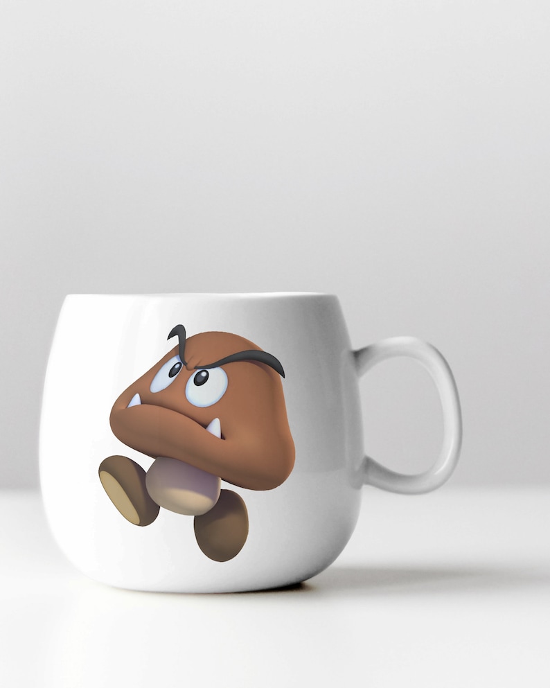 Peut inclure: Une tasse en c&eacute;ramique blanche avec un personnage de champignon de dessin anim&eacute; brun avec un visage renfrogn&eacute; et des dents pointues. Le personnage du champignon porte un sourcil noir.