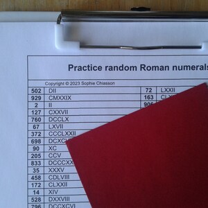 Puede incluir: Un portapapeles blanco con una carpeta roja encima. El portapapeles tiene una hoja de papel con una lista de números y sus equivalentes en números romanos. El texto en el papel dice "Practice random Roman numerals" y "Copyright © 2023 Sophie Chiasson".