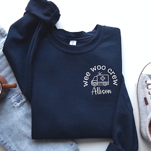 May include: A navy blue sweatshirt with a white graphic of an ambulance and the text "wee woo crew Allison".