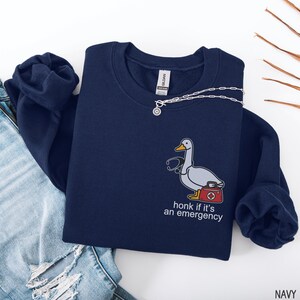 May include: Navy blue sweatshirt with a cartoon duck wearing a stethoscope and carrying a first aid kit. The text "honk if it's an emergency" is below the duck. A silver necklace is draped across the sweatshirt.