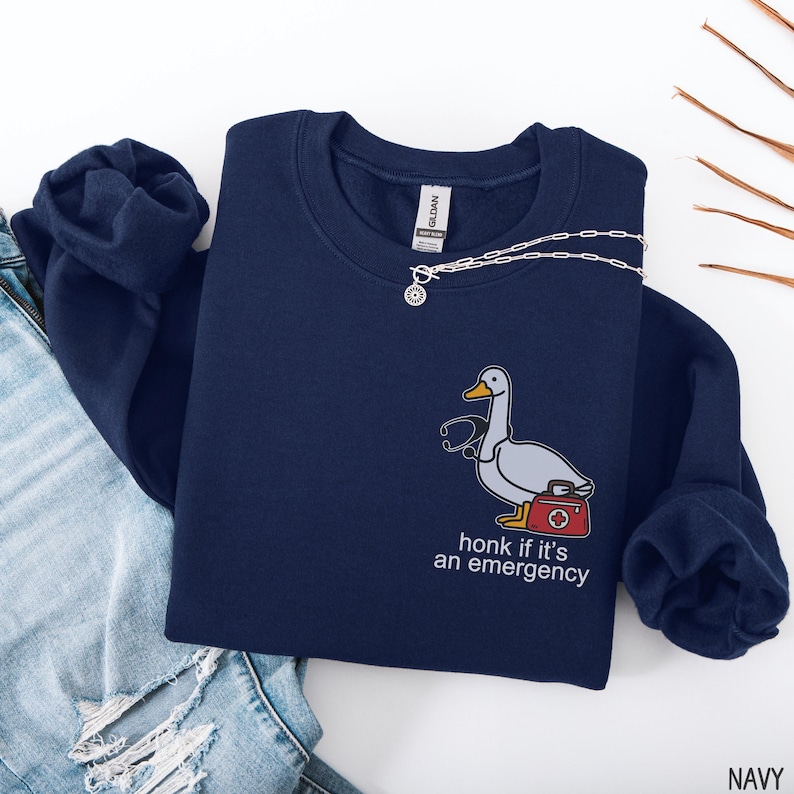 May include: Navy blue sweatshirt with a cartoon duck wearing a stethoscope and carrying a first aid kit. The text "honk if it's an emergency" is below the duck. A silver necklace is draped across the sweatshirt.