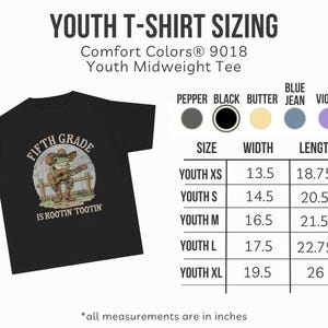 Puede incluir: Una camiseta negra para j&oacute;venes con el gr&aacute;fico de una rana con sombrero de vaquero y botas tocando la guitarra, con el texto FIFTH GRADE IS ROOTIN' TOOTIN'. Una tabla de tallas muestra medidas de ancho y largo en pulgadas de la XS a la XL.