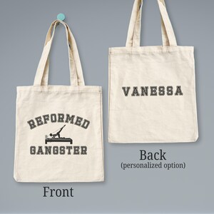 Pu&ograve; includere: Una borsa tote in tela bianca con testo nero. La parte anteriore della borsa dice "Reformed Gangster" con una silhouette di una persona che fa un esercizio di pilates. La parte posteriore della borsa ha il nome "Vanessa" in testo nero.