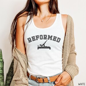 May include: White tank top with the text "REFORMED" in black letters with a black silhouette of a person on a reformer pilates machine.