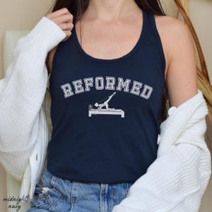 May include: A navy blue tank top with the text "REFORMED" in white, with a white silhouette of a person on a reformer pilates machine.