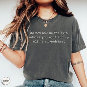 Peut inclure: Un t-shirt gris anthracite à manches courtes avec le texte blanc "do not ask me for life advice you will end up with a spreadsheet" imprimé sur la poitrine. Le t-shirt présente une encolure ronde et une coupe décontractée en coton doux.