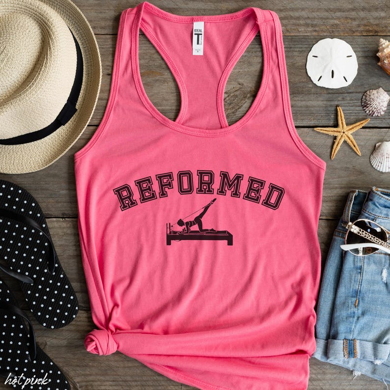 May include: Pink tank top with a black graphic of a person doing a reformer pilates exercise. The text "REFORMED" is above the graphic.