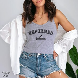 May include: A heather grey tank top with the text "REFORMED" in black lettering. A silhouette of a person doing a pilates exercise is printed on the tank top.