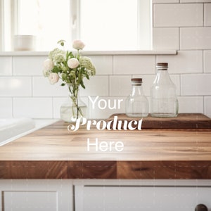 Puede incluir: Una encimera de madera con un salpicadero de azulejos blancos. Hay dos botellas de vidrio transparente con tapas de corcho y un ramo de flores blancas en un jarrón de vidrio transparente. El texto "Your Product Here" está superpuesto en la encimera.