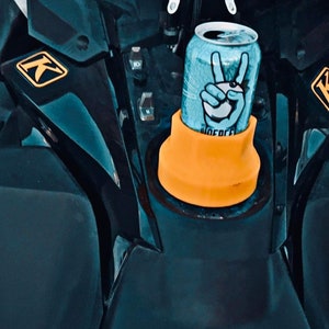 May include: A black motorcycle with a yellow K logo and a yellow cup holder. A blue can with a peace sign logo is in the cup holder.