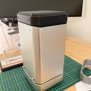 Könnte beinhalten: Ein silbernes und schwarzes Computergehäuse mit einer strukturierten Oberseite und einem schwarzen Netzschalter an der Vorderseite.