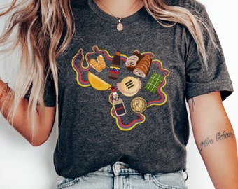 May include: A dark gray t-shirt with a graphic design of a map of Venezuela with various Venezuelan foods and drinks. The foods include arepas, tequeños, hallacas, and a bottle of rum. The text "Mio Océan" is tattooed on the person's arm.