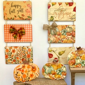 May include: Two vertical hanging wall signs featuring autumn themes with text reading happy fall y'all and welcome autumn, accompanied by three pumpkin-shaped wooden cutouts decorated with floral patterns and assorted pumpkin illustrations.