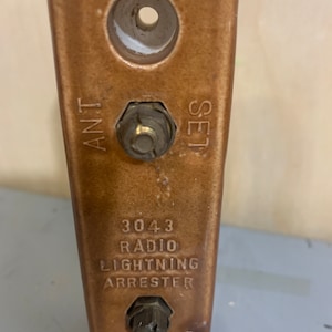 Puede incluir: Un pararrayos de radio de cerámica marrón con el número de modelo 3043 impreso en él. El pararrayos tiene dos terminales metálicos etiquetados como "ANT" y "SET".