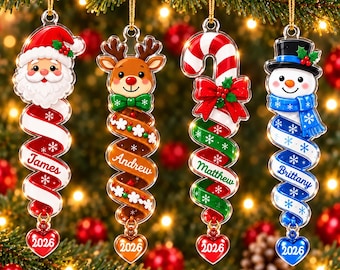 May include: Four hanging Christmas ornaments featuring Santa, a reindeer, a candy cane, and a snowman. Each ornament has a spiral tail with a name, James, Andrew, Matthew, or Brittany, and a heart-shaped charm at the bottom labeled with the year 2026.