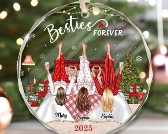 May include: A clear, round Christmas ornament with the words "Besties Forever" and the year 2025. The ornament features an illustration of four people in pajamas on a bed, with a Christmas tree and gifts in the background.